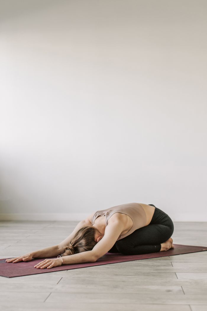 A woman practicing yoga in child's pose on a mat indoors, promoting relaxation and wellness.