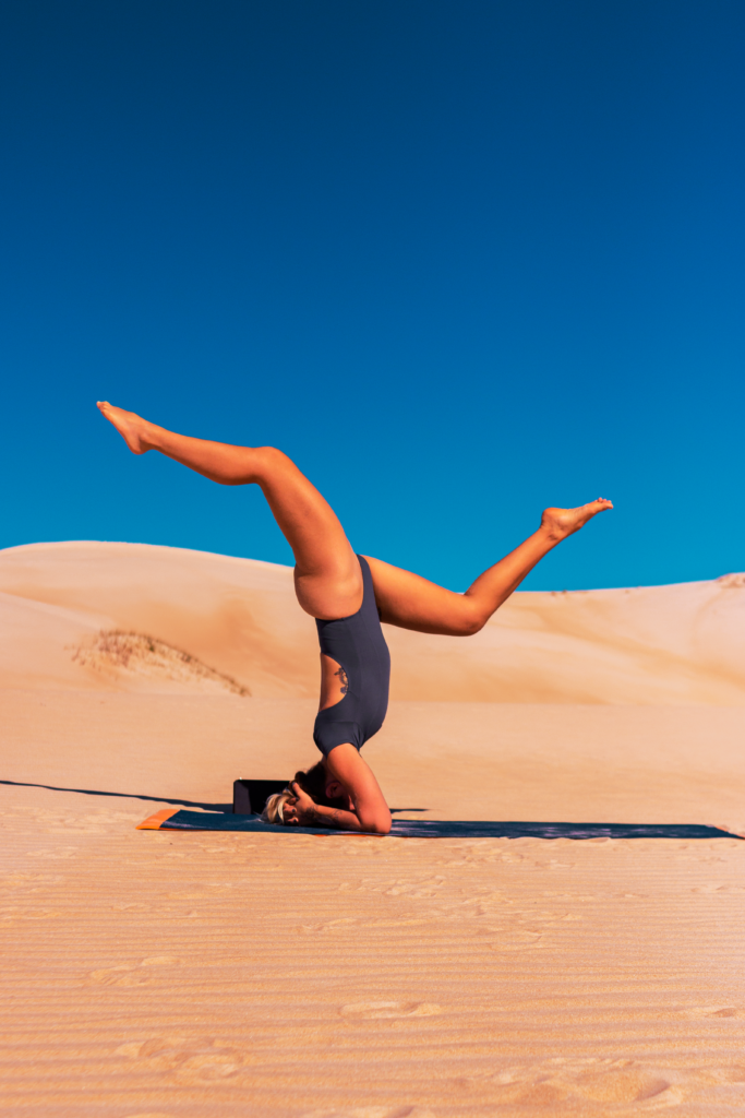Woman performing yoga on sand dunes in Garopaba, Brazil, under a clear blue sky.